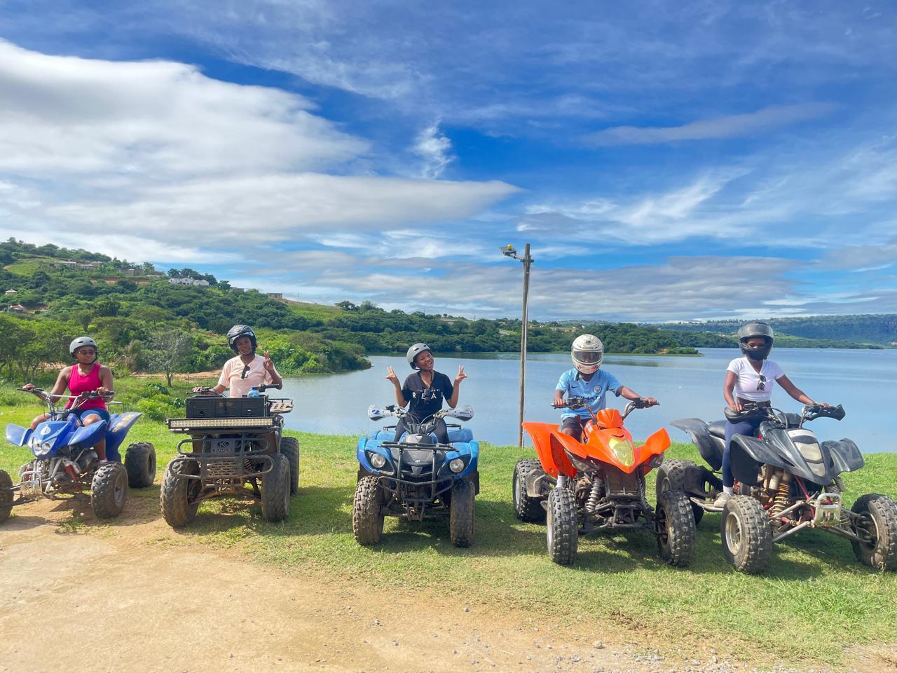 A group of smiling quad bikers posing with Inanda Dam in the background